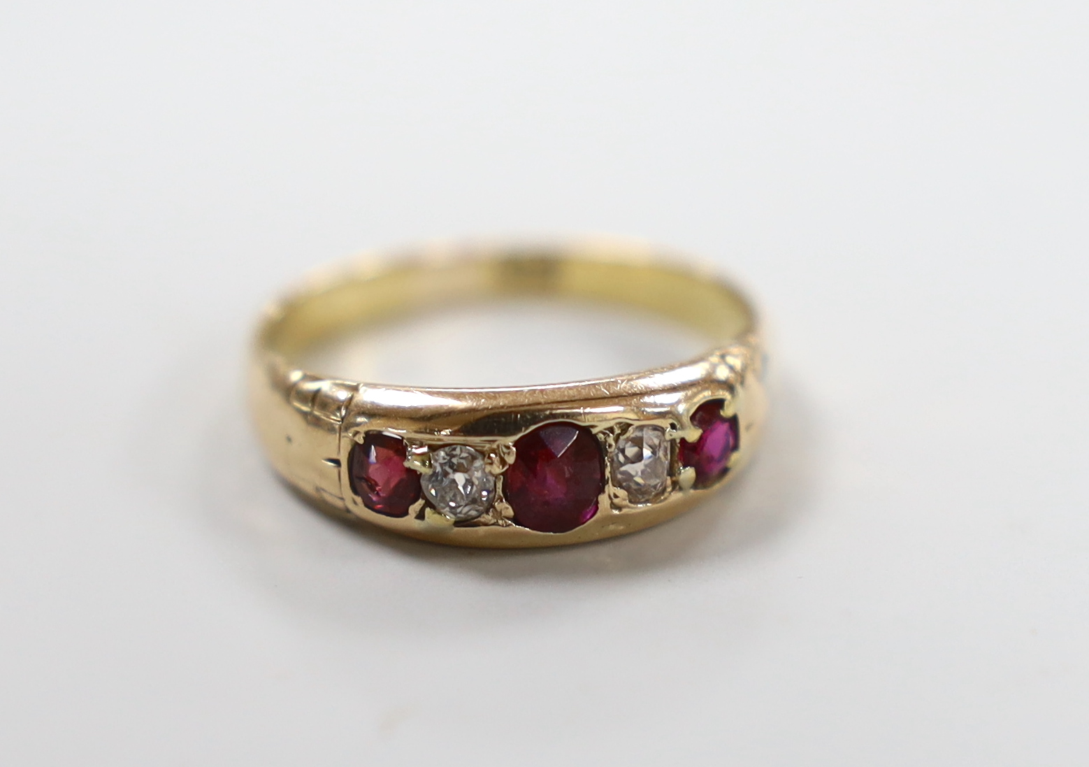 An 18ct and gypsy set three stone ruby and two stone diamond half hoop ring, size Q, gross weight 3.3 grams.